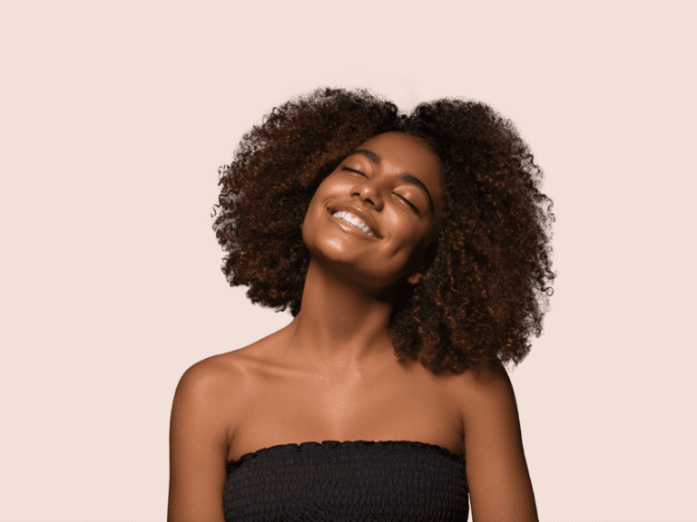 A black hair stylist with afro hair smiling on a beige background.