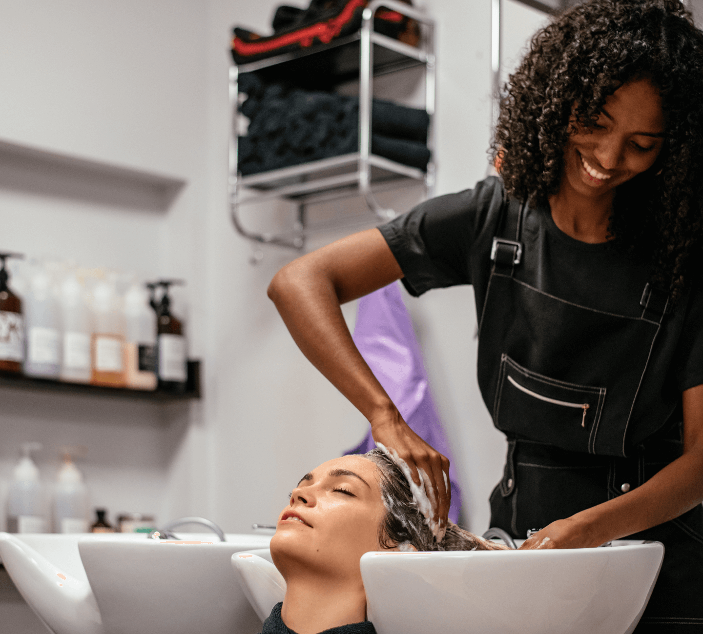 A black woman getting her hair done by a stylist in a salon.