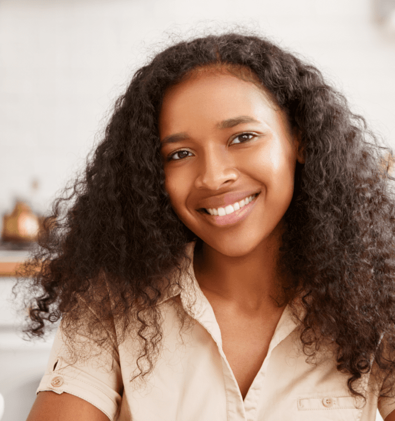 A young African American woman with curly hair smiling in the kitchen, showcasing her black hair.