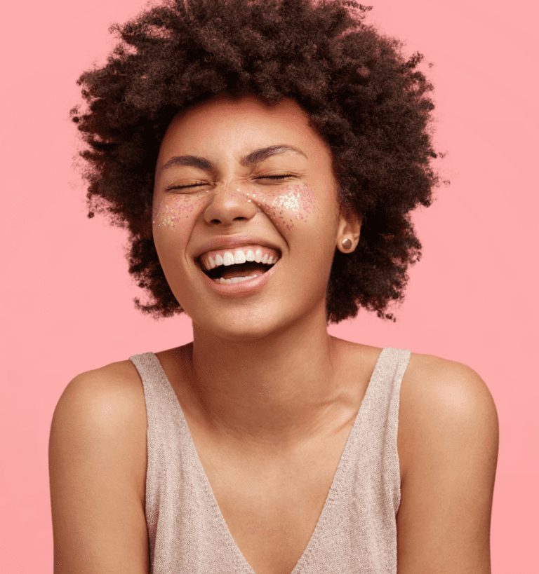 A black hairstylist with afro hair laughing on a pink background.