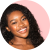 A black hairstylist with curly hair smiling in front of a pink background.